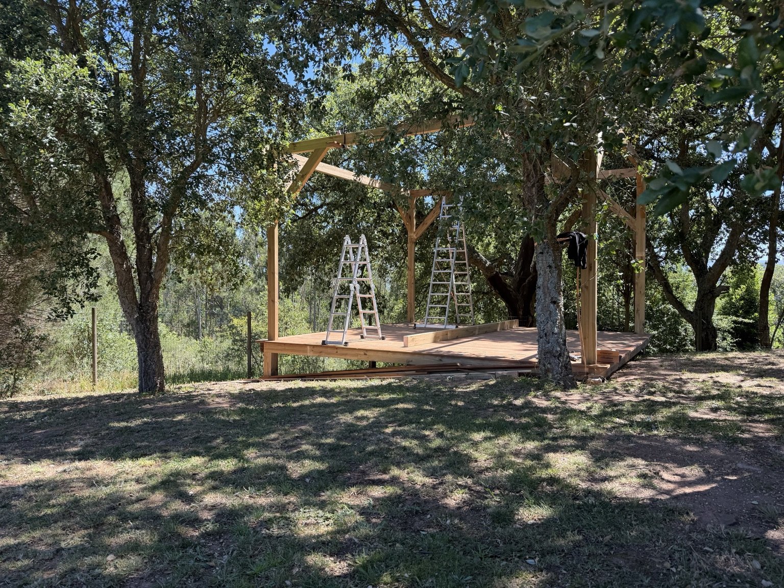 Outdoor gathering platform under construction beneath mature trees